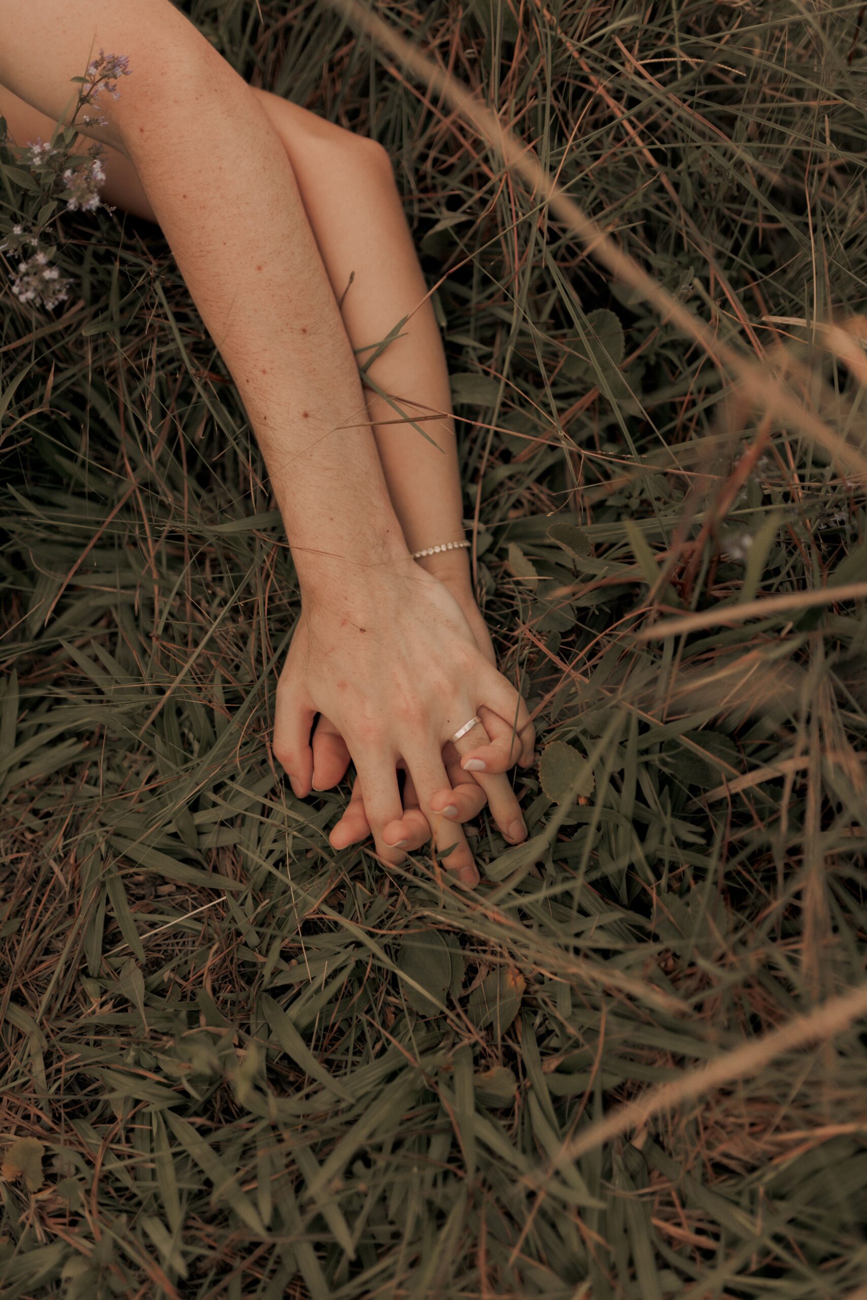 Couple holding hands in grassy field, capturing intimacy and connection.