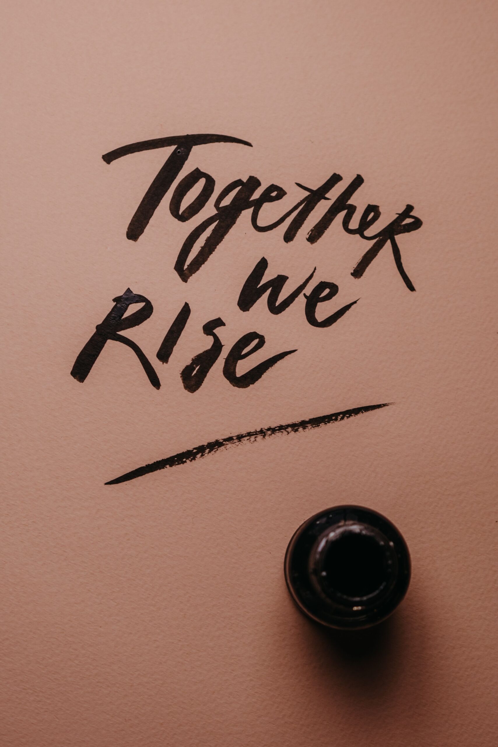Artistic hand lettering 'Together we rise' with ink on a pink background for motivation.